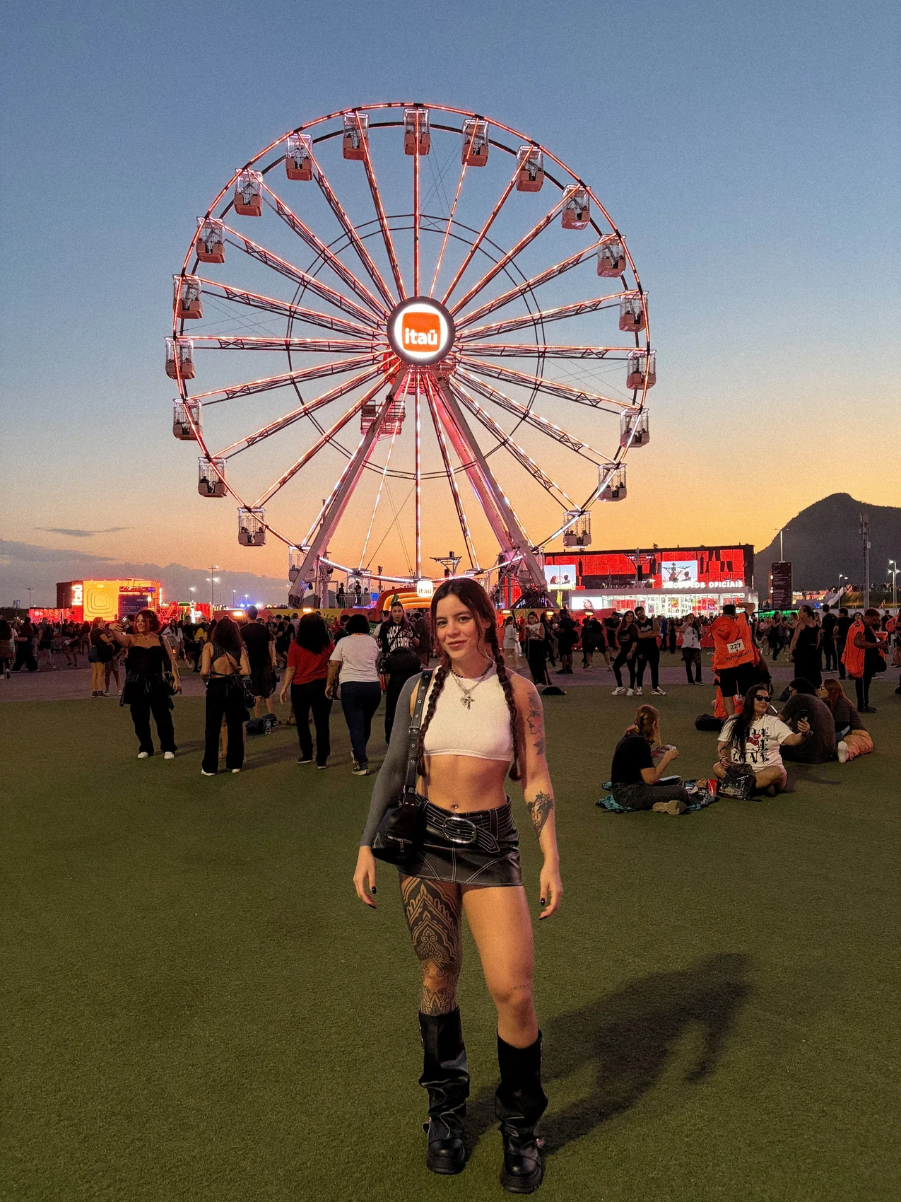 Adri em foto de corpo inteiro em festival diante de uma roda gigante